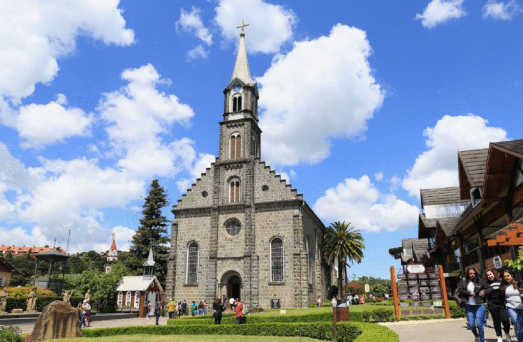 Fachada frontal da Igreja Matriz São Pedro em Gramado, com torre de pedra, vitrais e estátua de São Pedro ao lado