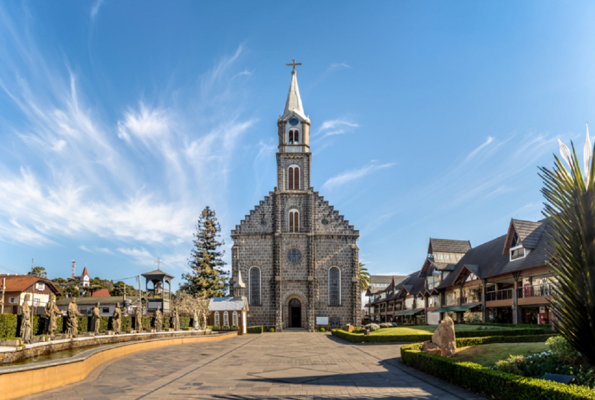 Rua em frente à Igreja Matriz São Pedro em Gramado, com calçamento de pedra, flores nos canteiros e a igreja ao fundo